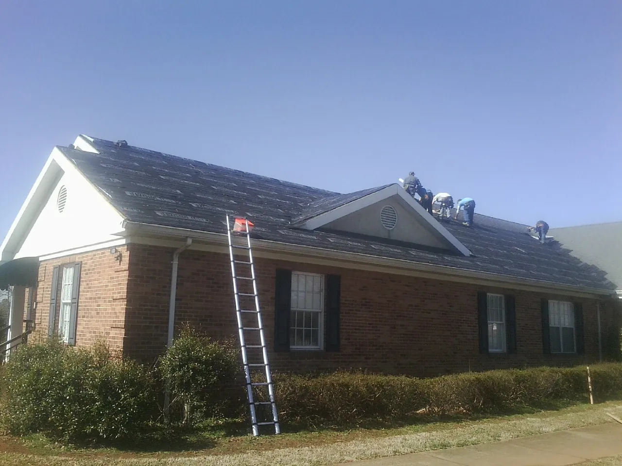 Crew tearing shingles off a brick ranch roof with a ladder set — Metal Roof Repair work by our crew in Belden