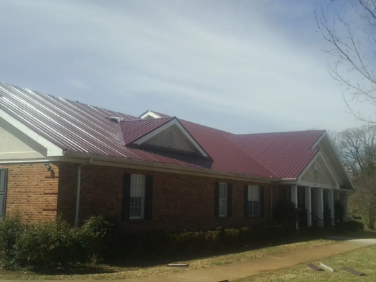Red metal roof with gabled entries on a long brick building, from a Hail Damage Roof Repair job in Belden
