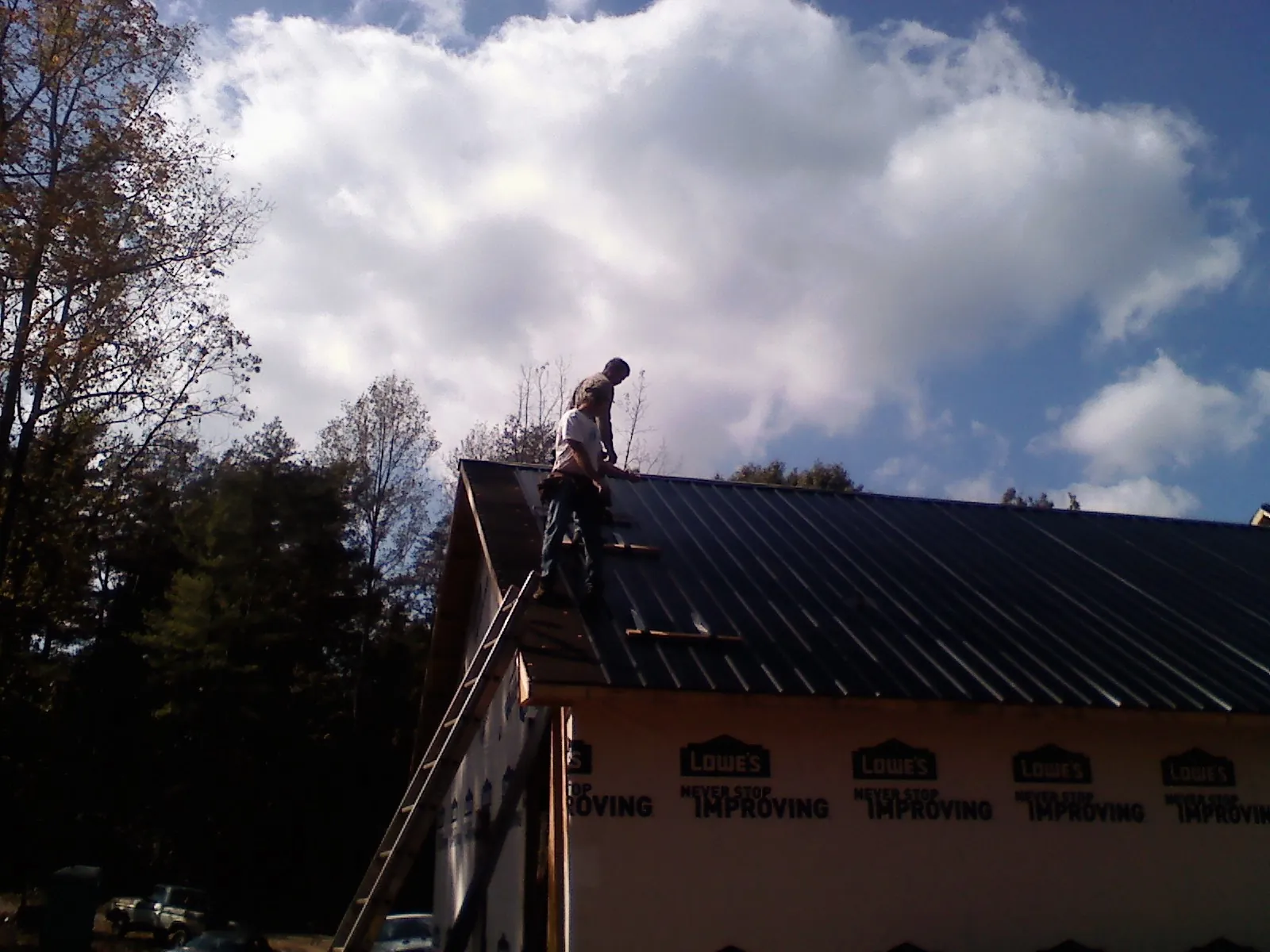 Roofer fastening dark metal panels high against a cloudy sky, from a Roof Inspection job in Belden