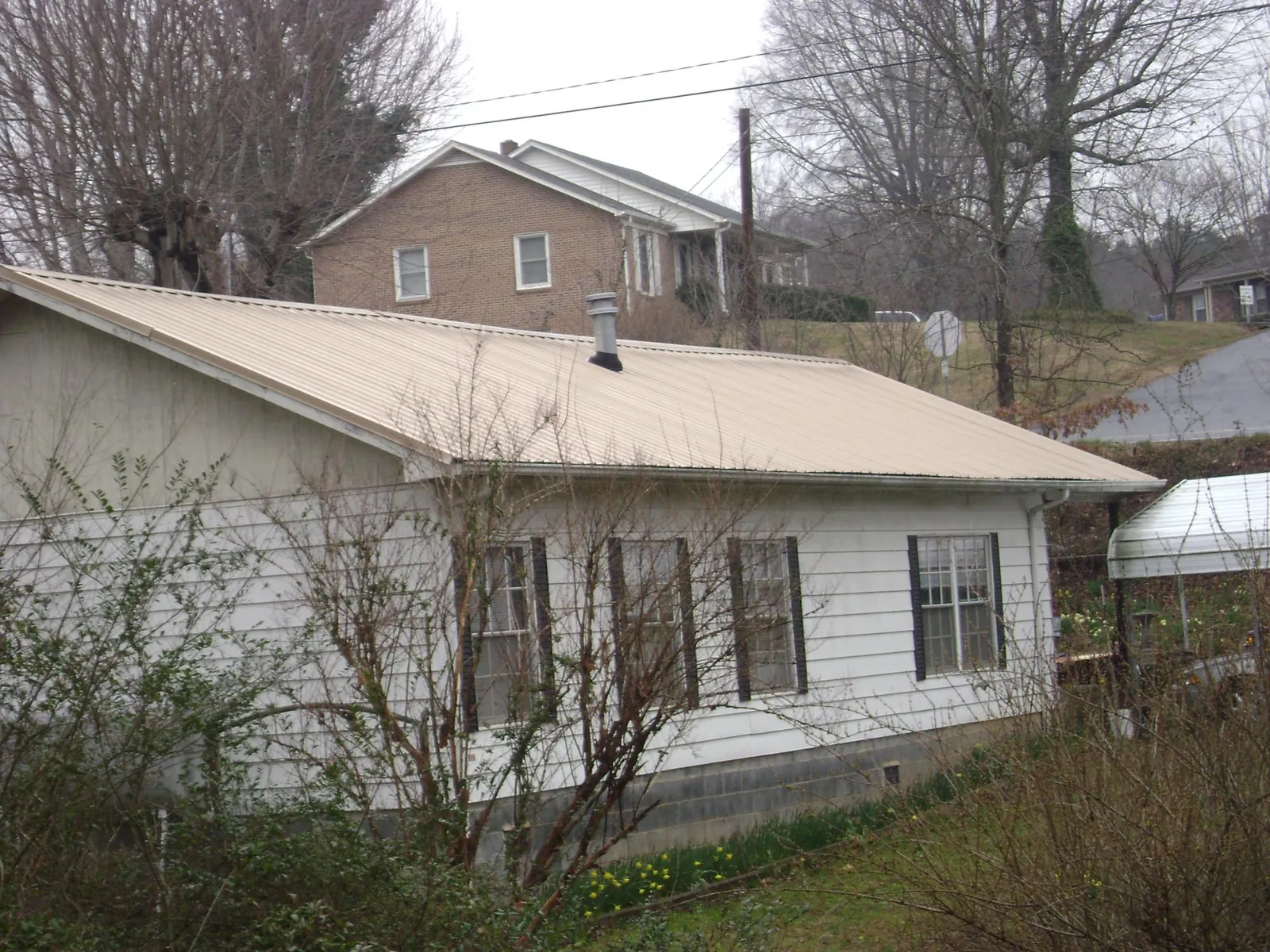 Tan metal roof on a white sided house set into a hillside — Commercial Roofing by Roofing Brothers in Belden